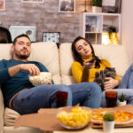Beautiful young couple watching TV and eating fast food takeaway