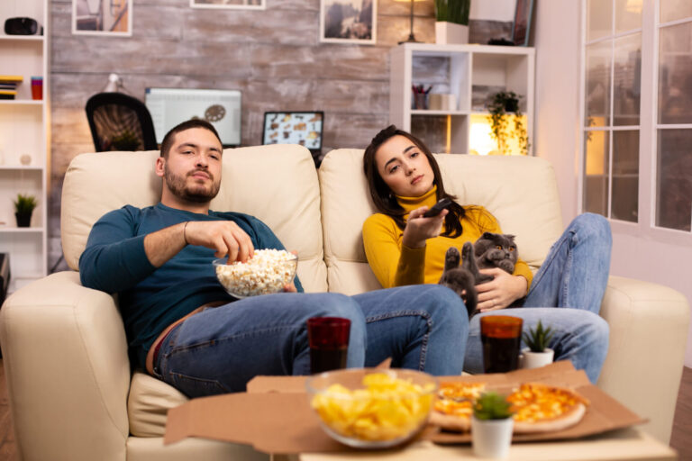Beautiful young couple watching TV and eating fast food takeaway