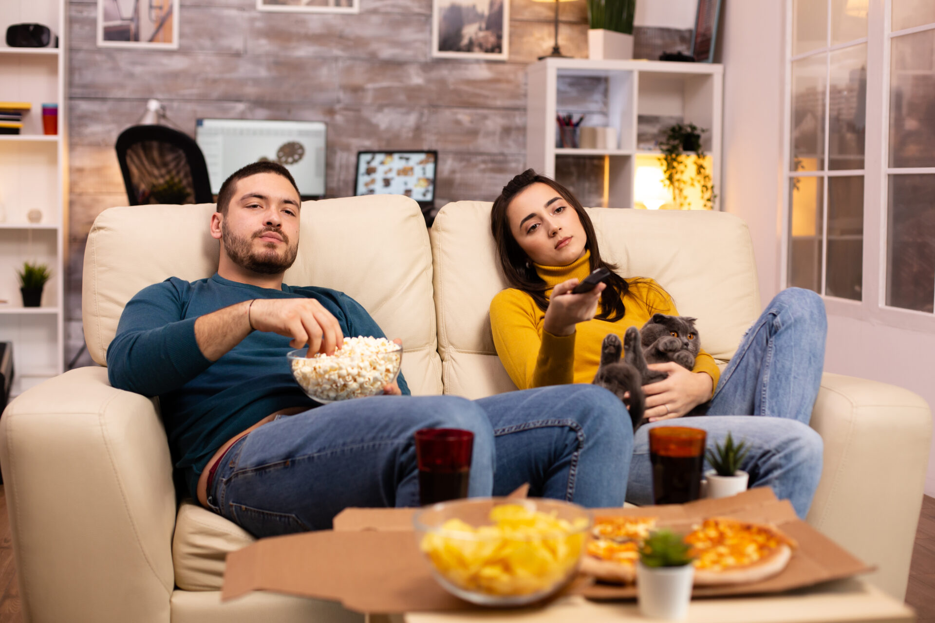 Beautiful young couple watching TV and eating fast food takeaway